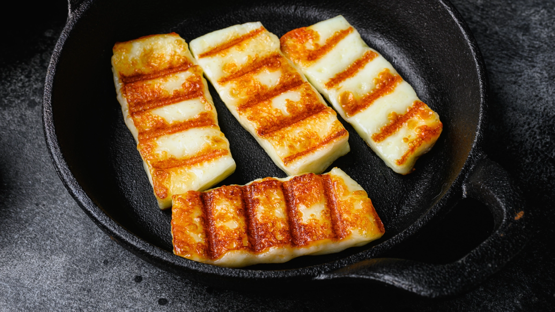 An iron frying pan with four slightly toasted slices of halloumi.