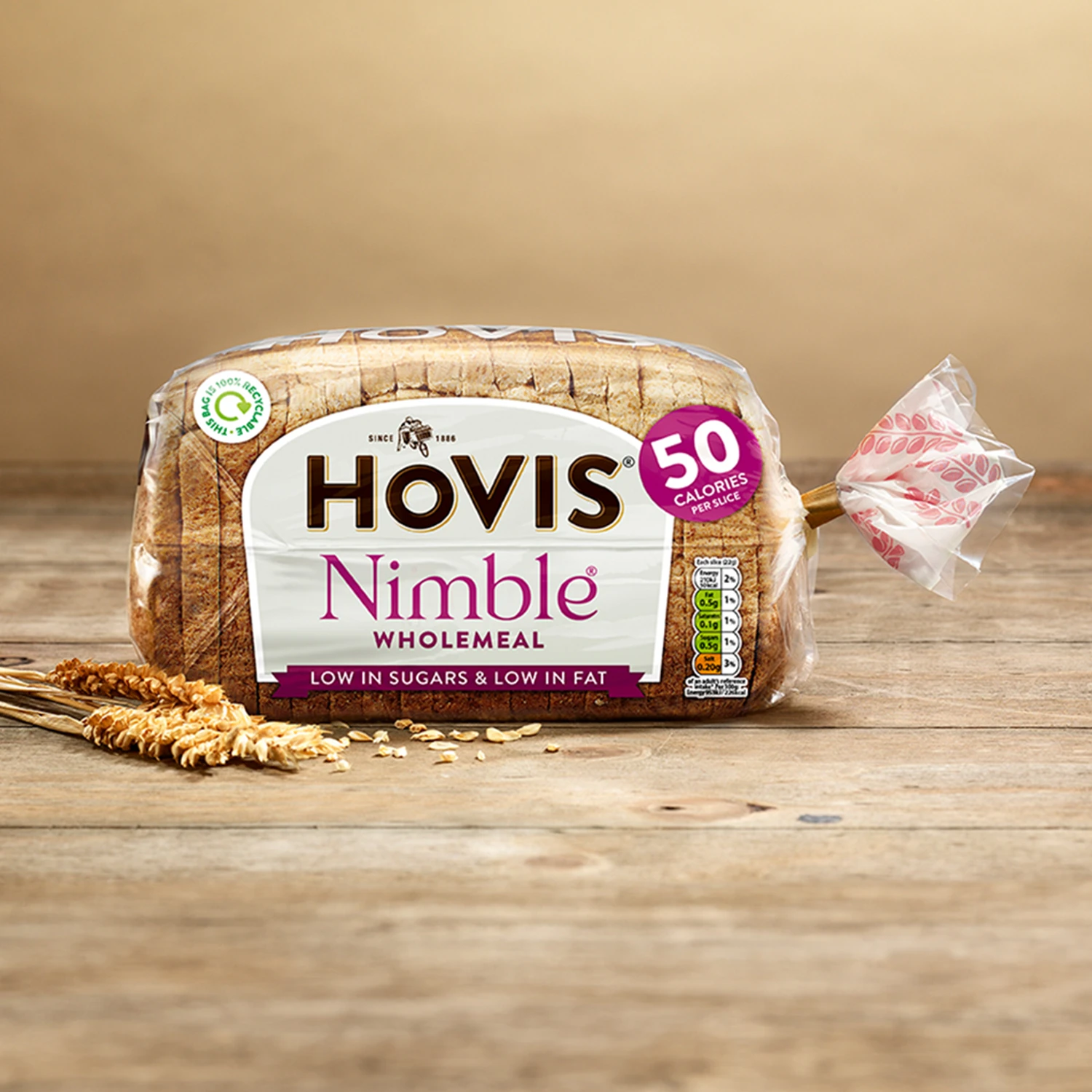 Hovis Nimble Wholemeal bread against a light beige background on a wooden table, with a couple of dried wheat stalks on the left.