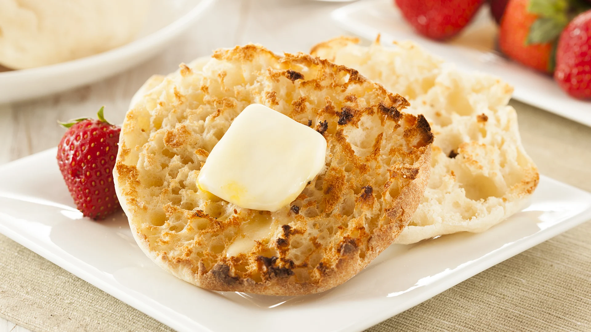 A pack of Hovis Farmhouse Cheddar Muffins is placed on a rustic wooden table, set against a dark grey background.