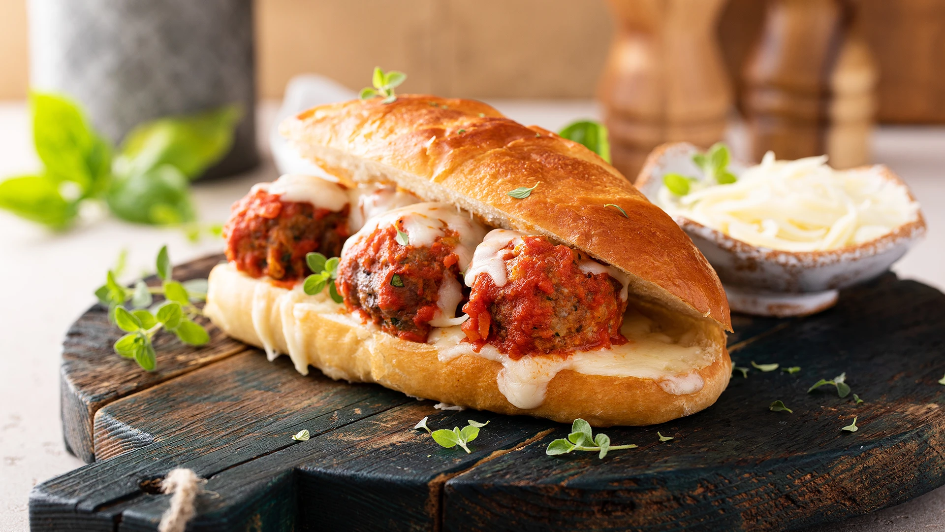 A lovely full Beef Meatball Sub with tomato sauce, pesto and mozzeralla sits on a wooden chopping board on a kitchen counter