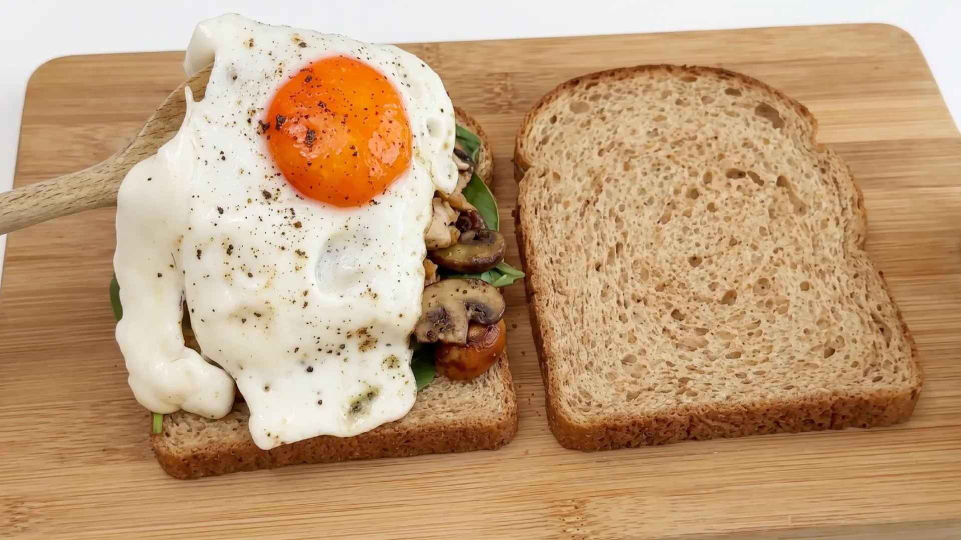 An open-faced breakfast sandwich on whole wheat bread topped with sausage, mushrooms and a seasoned fried egg.