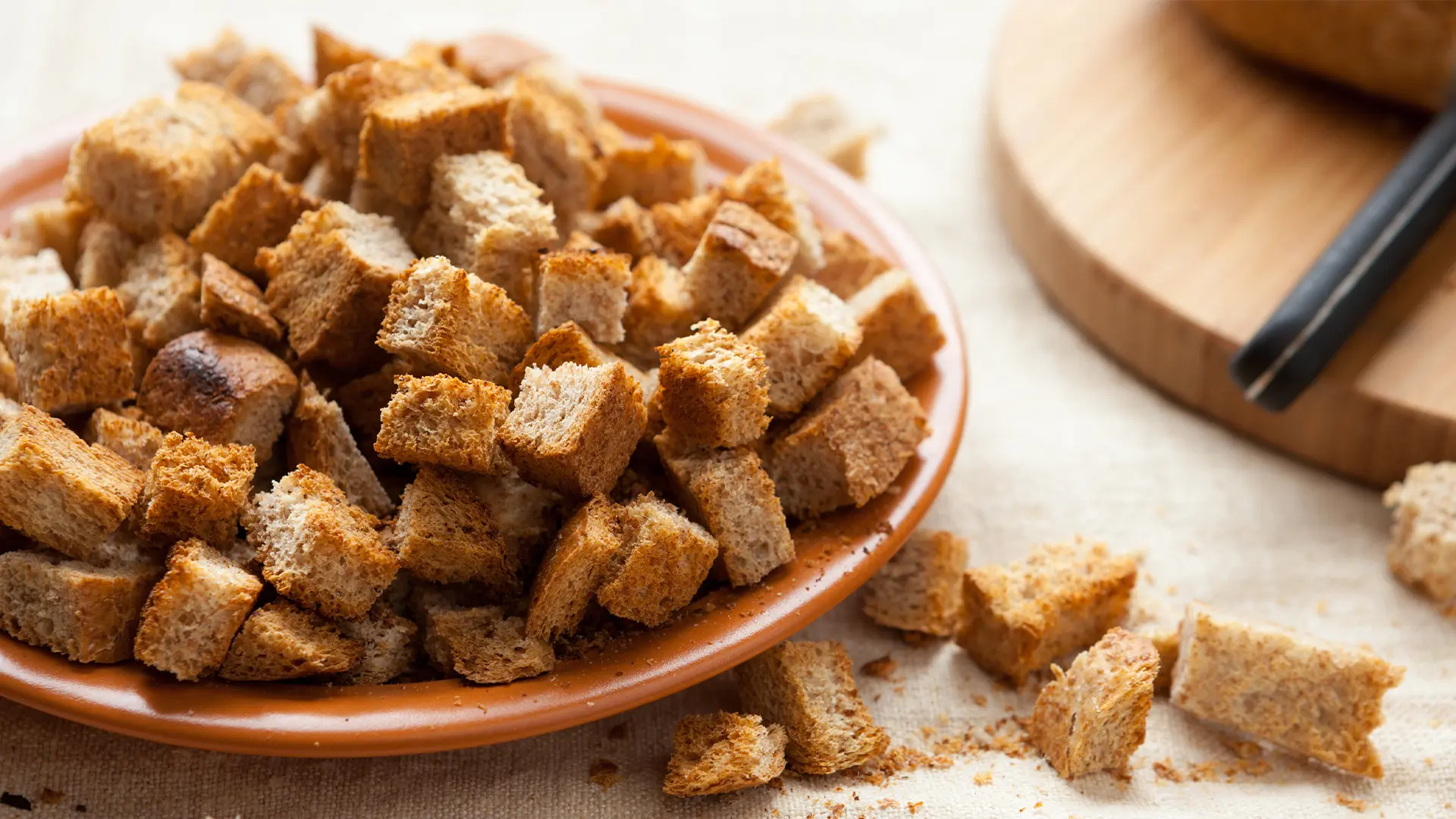 Close-up of a plate filled with small toasted bread cubes, with some pieces scattered on the tablecloth nearby