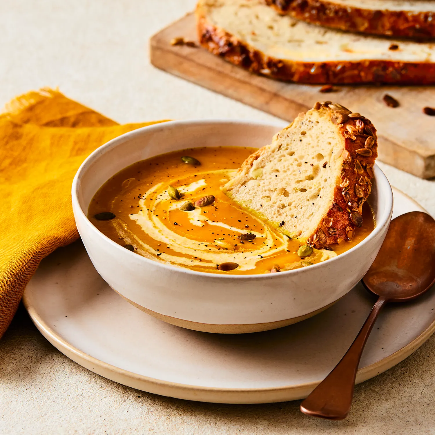 A close-up image of a Hovis®  Seeded Sourdough slice in a bowl of Butternut Squash Soup with extra Seeded Sourdough Slices in the background