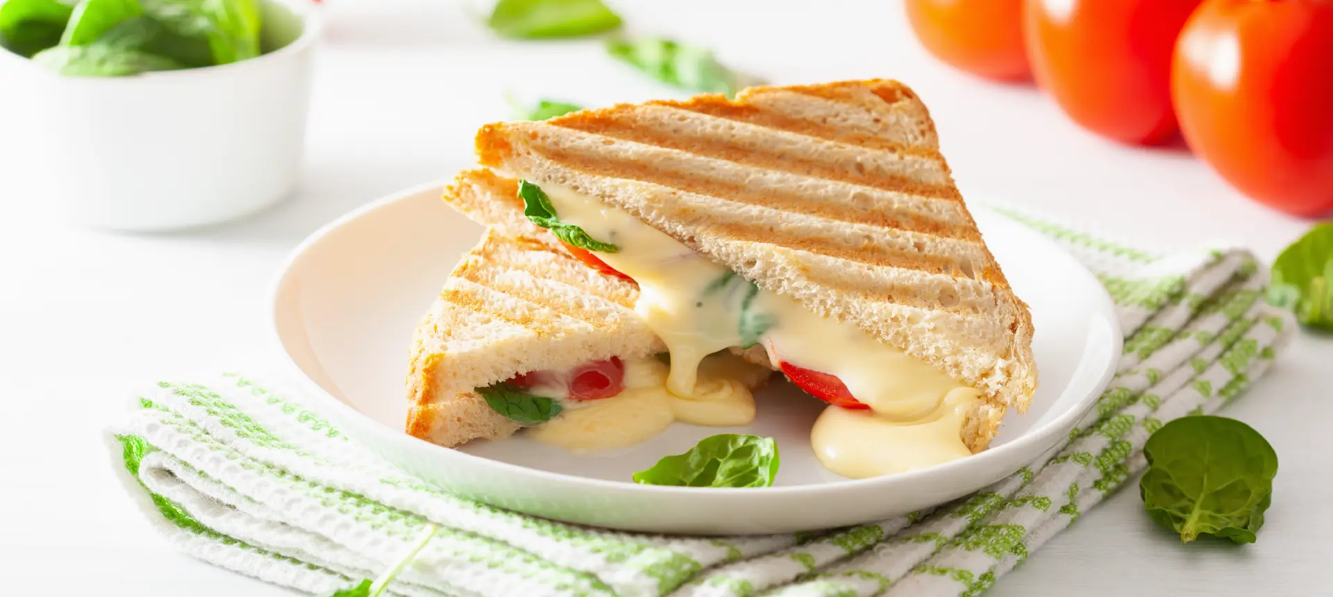 A toastie made with Hovis Nimble Danish White bread, cut in half and filled with molten cheese, basil leaves, and thinly sliced tomatoes.