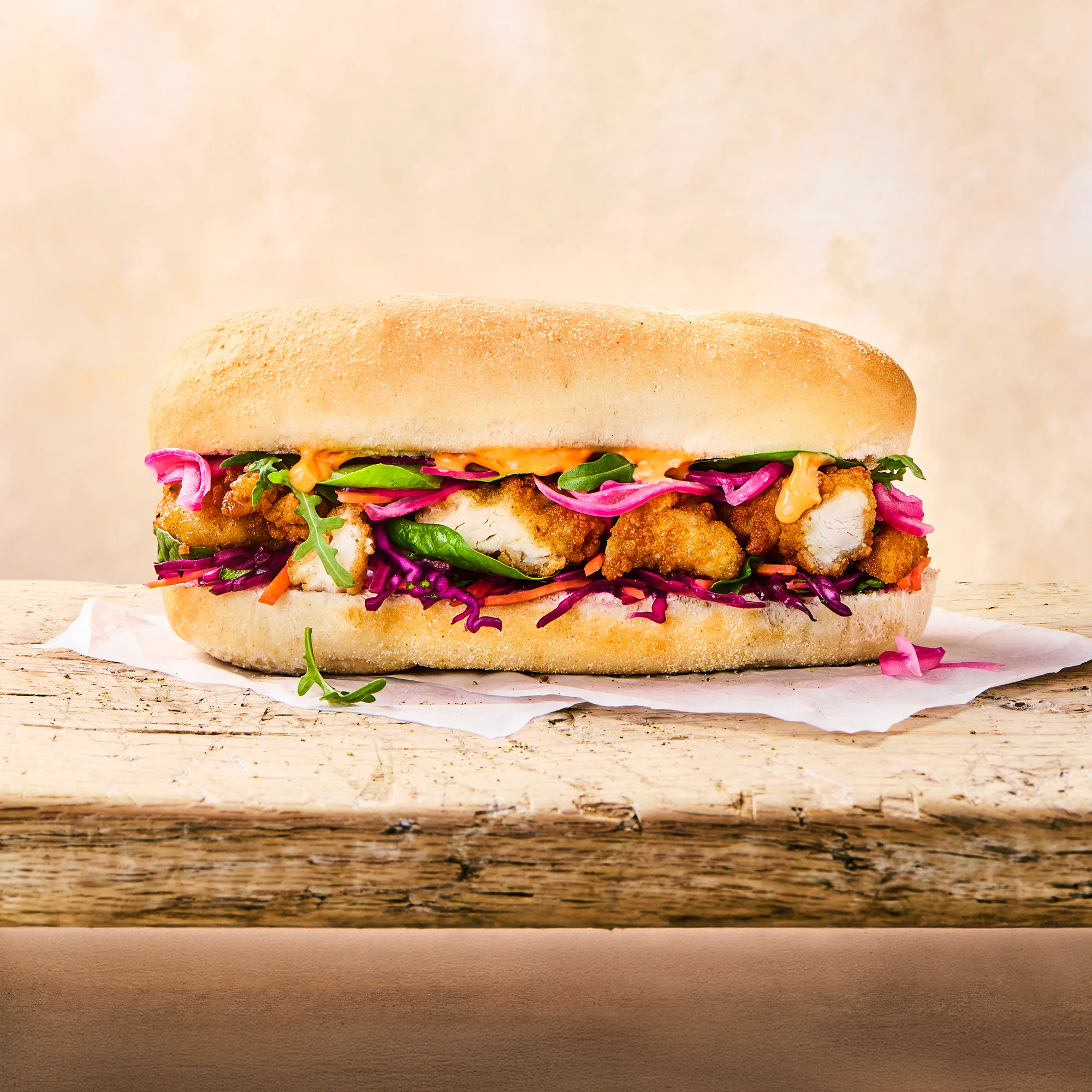 A delicious Cajun subroll sits on a wooden table with a cloth, you can see asian slow poking through the roll. 