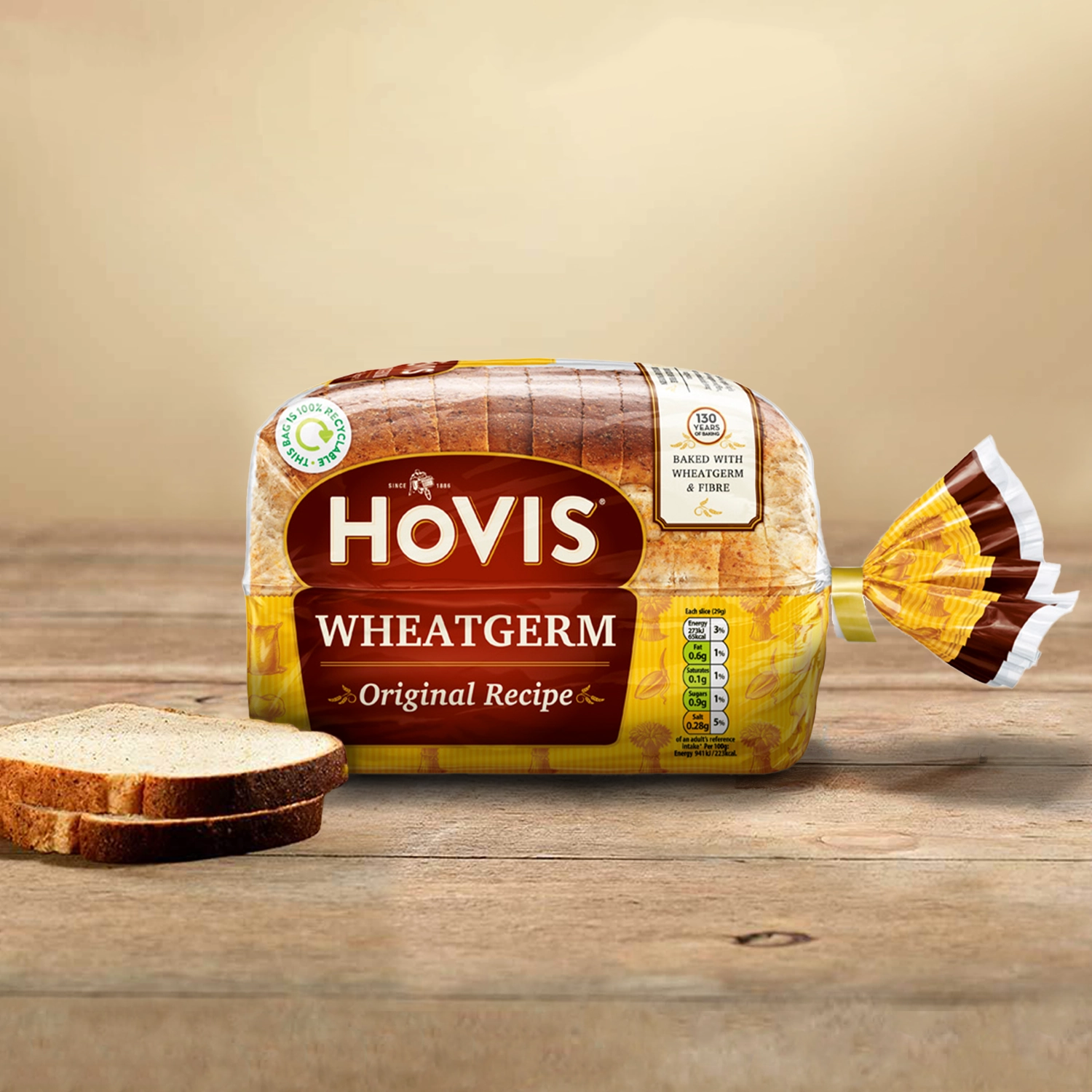 Hovis Tasty Wholemeal 400g bread against a light beige background on a wooden table, with two stacked slices of bread on the left.