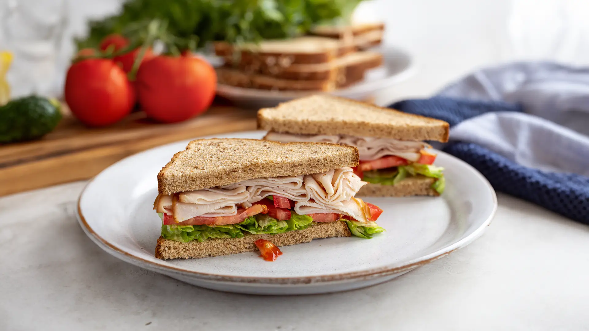 A sandwich sliced in half, filled with ham, tomatoes and green salad leaves.