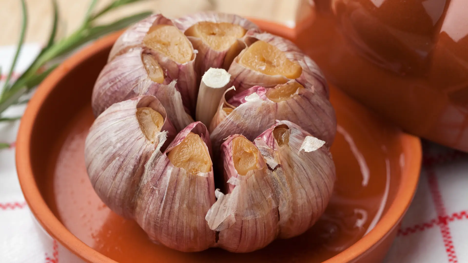 A whole head of roasted garlic with the top cut off, exposing golden cloves, served in a small terracotta dish.