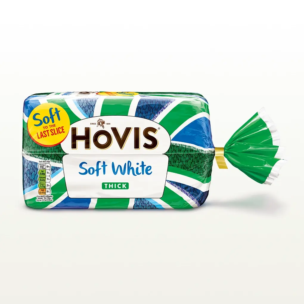 Hovis Soft White Thick Sliced bread on a white backdrop with a subtle shadow. The packaging features a green Union Jack pattern and a yellow label reading 'Soft to the Last Slice.'