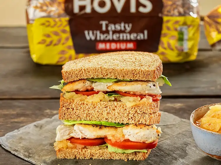 A sandwich cute in half sits on a plate, it contains chicken, lettuce, tomatoes and pineapple jam.