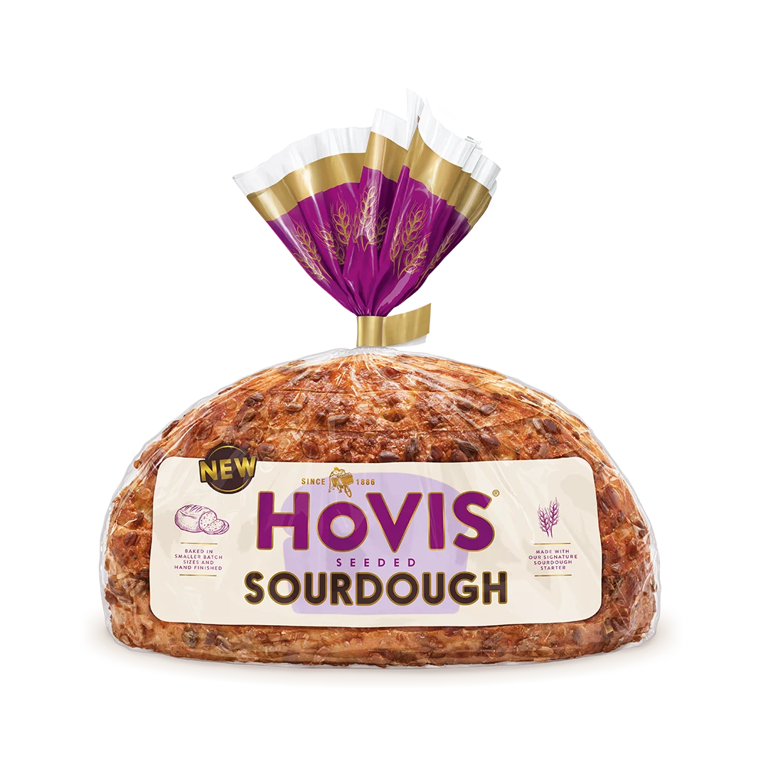 Hovis Seeded Sourdough bread on a white backdrop with a subtle shadow. The packaging is half transparent and half light and dark purple with gold detailing