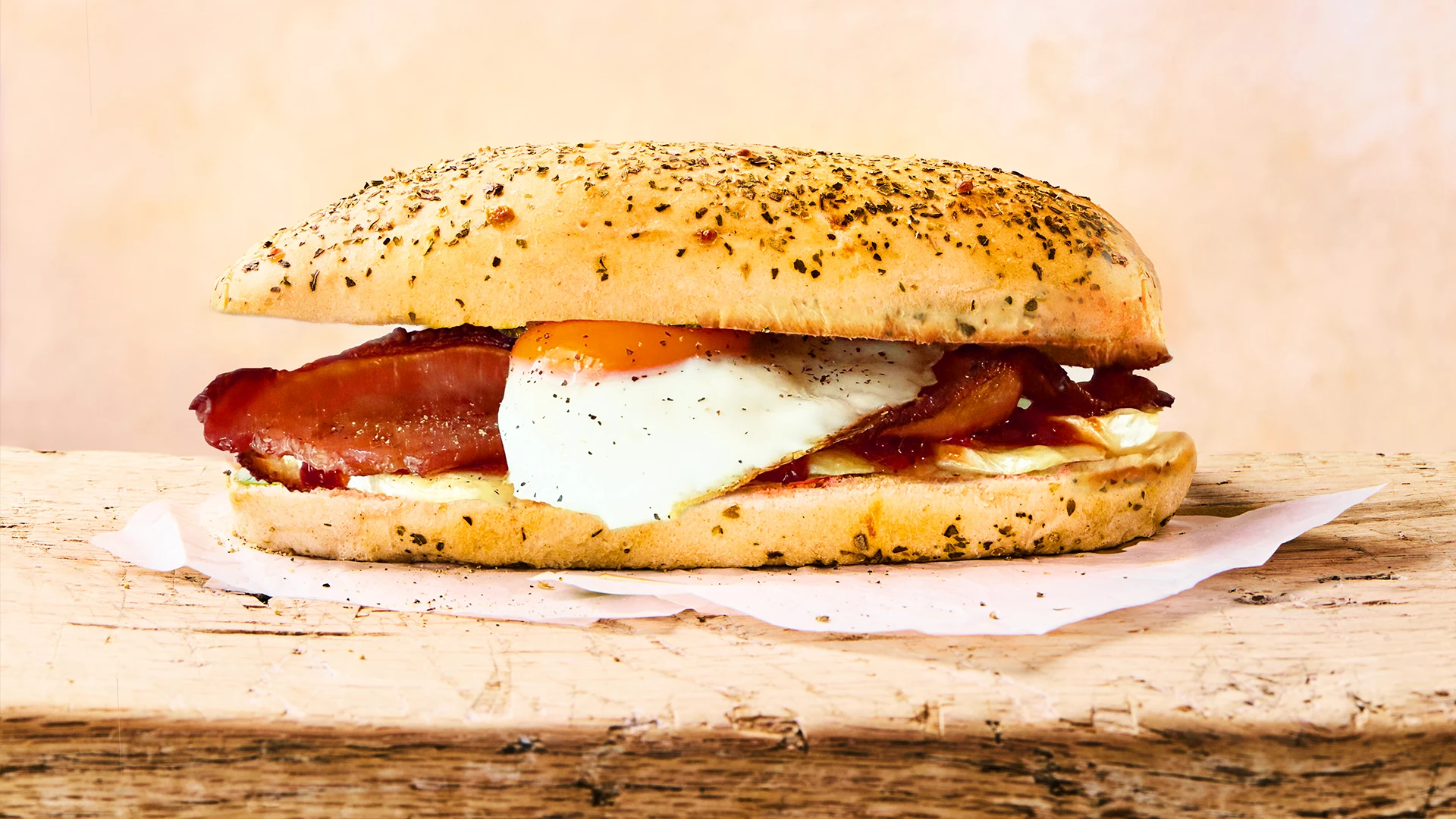 a complete Melted Brie & Chilli Jam Sandwich sits on a white plate next to some extra slices of brie cheese. The plate sits on a blue and white striped tea town on a marble kitchen counter 