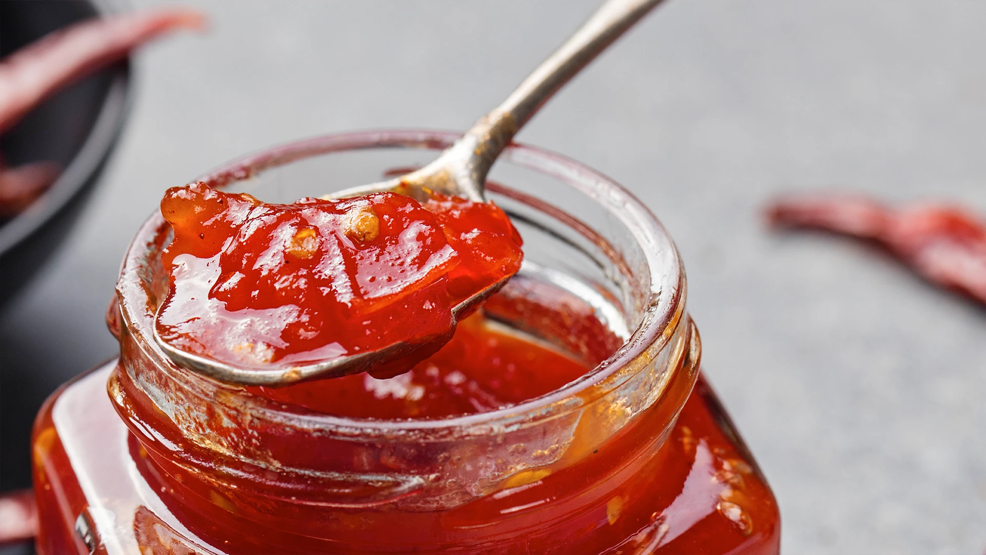 A close up on a jar of chilli jam with a spoon scooping some out 
