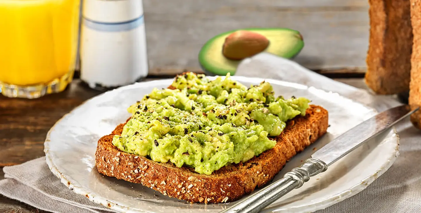A slice of Hovis Granary Wholemeal with smashed avocado on top with a sprinkle of salt and pepper on top.