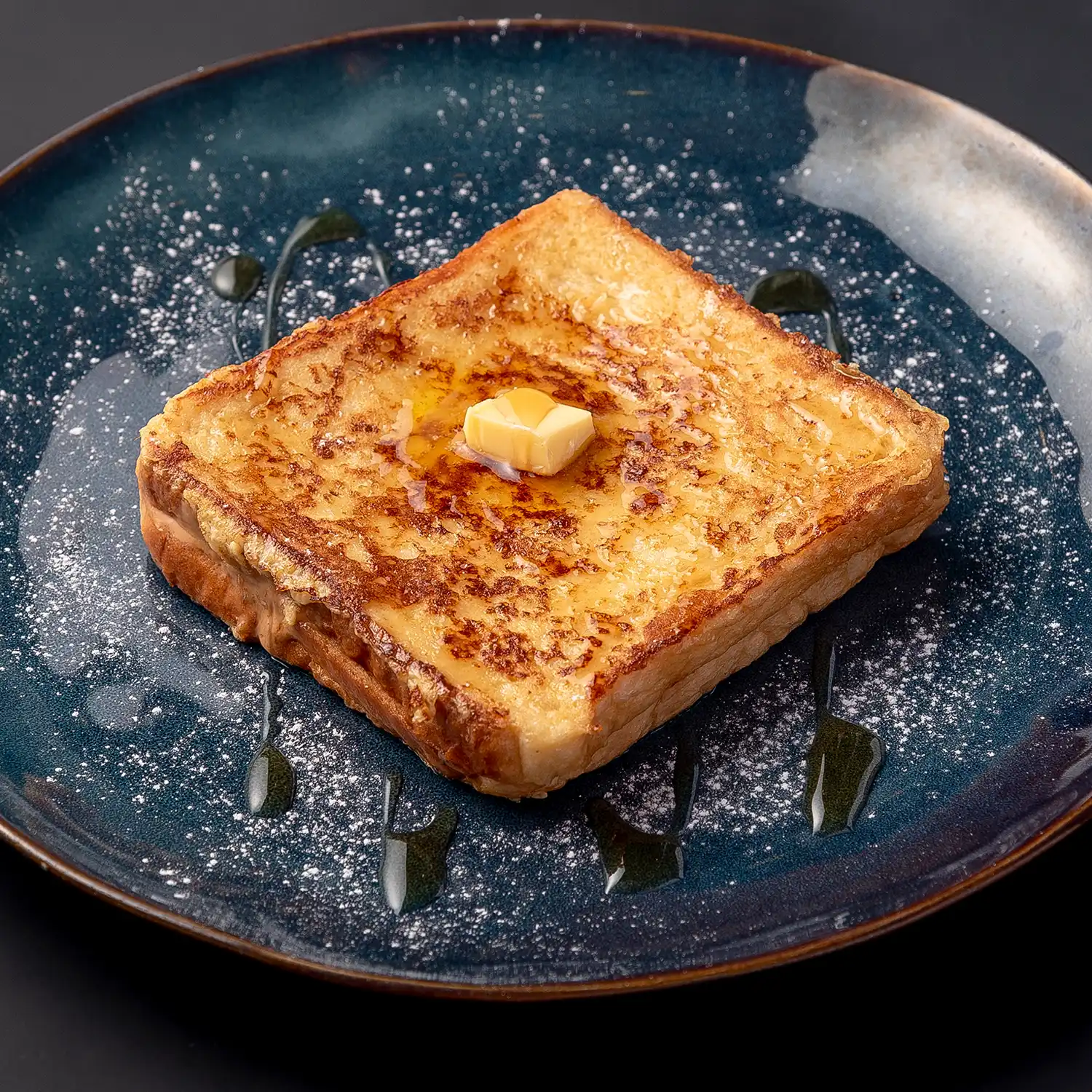 Close up of Hong Kong French toast on a blue plate, drizzled with golden syrup, dusted with icing sugar, and topped with a knob of butter.
