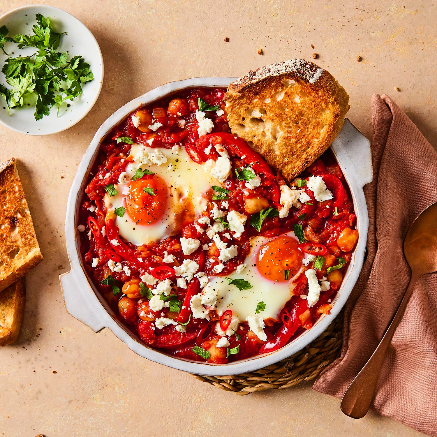 A close-up image of a Hovis®  White Sourdough slice in a pot of shakshuka, topped with two sunny-side-up eggs