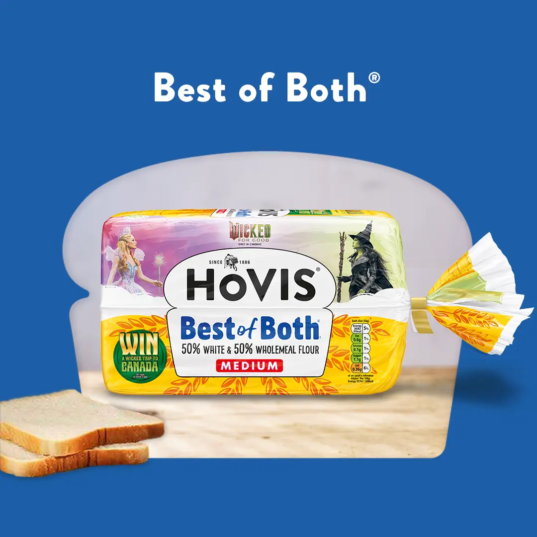 The text reads: Best of Both. A Hovis Best of Both loaf sits on a wooden table with a few slices of bread to the side. Its cropped into a loaf shape with a blue background. 