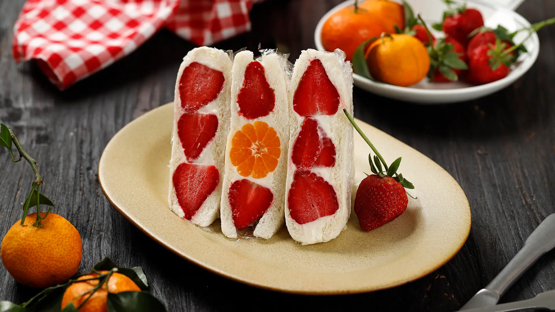 A light yellow plate with three half Hovis Soft White Medium Sliced sandwiches, each filled with halved strawberries and clementines, surrounded by cream.