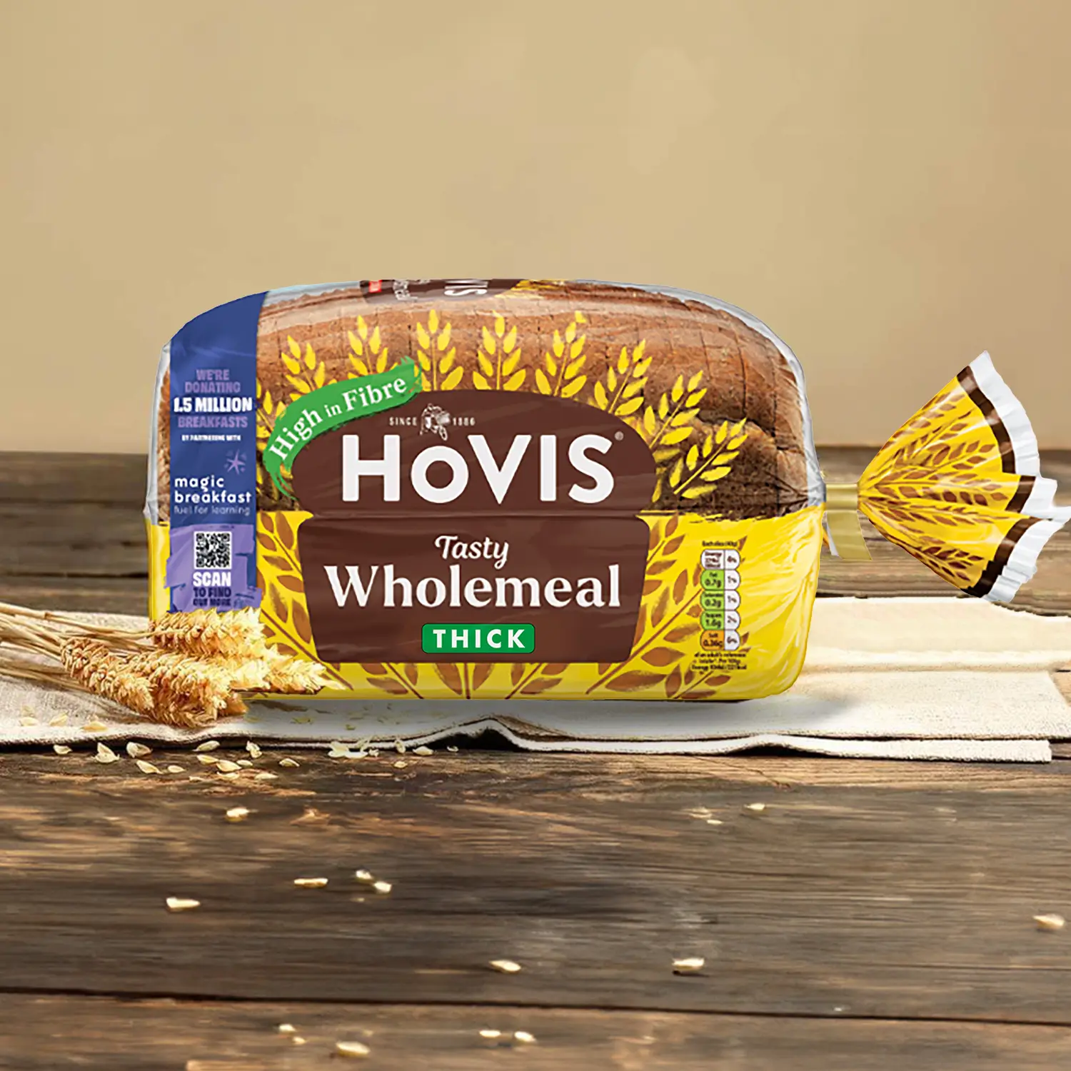 Hovis Tasty Wholemeal Thick Sliced bread on napkins against a light beige background atop a wooden table, surrounded by dried wheat.