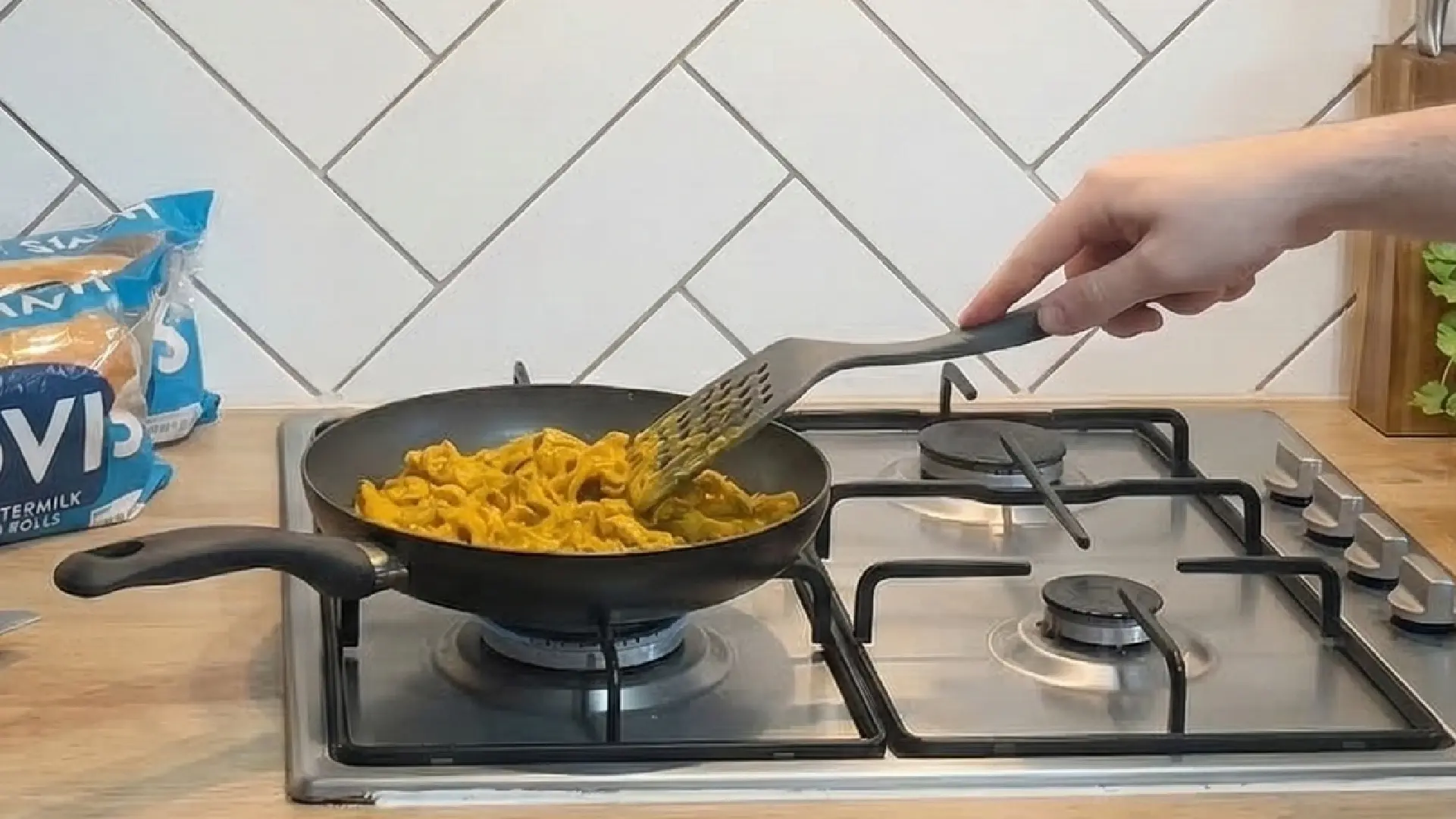 Satay sauce cooked chicken pieces being cooked in a pan on a hob. A packet of Hovis Sub Rolls is visible in the background. 