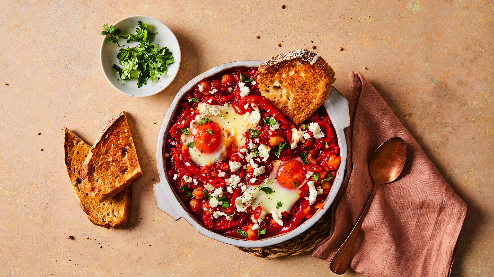 A close-up image of a Hovis®  White Sourdough slice in a pot of shakshuka, topped with two sunny-side-up eggs