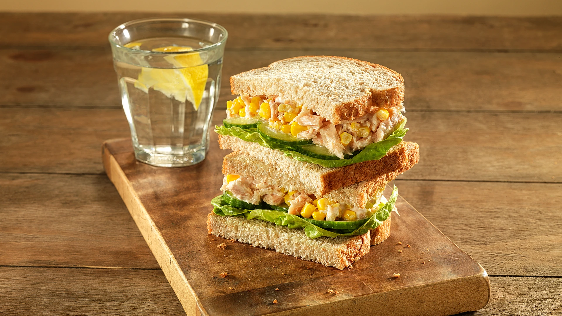 A delicious sandwich made with Hovis Wheatgerm bread, filled with fresh lettuce, sweetcorn, and tuna, on a wooden chopping board.