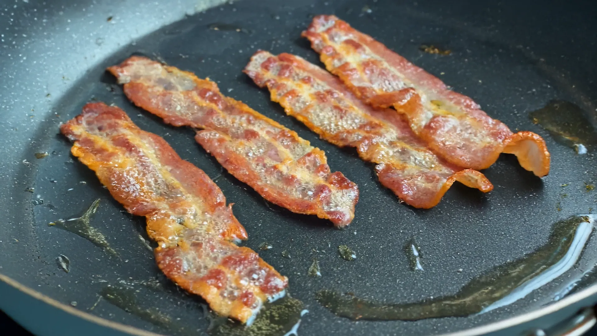  Close up image of bacon frying on an oiled pan 