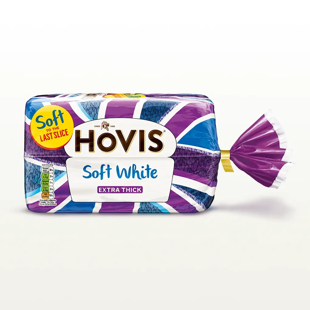 Hovis Soft White Extra Thick Sliced bread on a white backdrop with a subtle shadow. The packaging features a purple Union Jack pattern and a yellow label reading 'Soft to the Last Slice.'