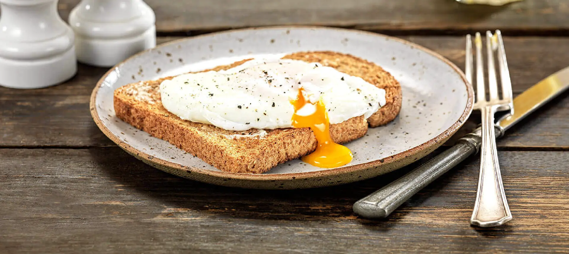 A slice of toasted Hovis Tasty Wholemeal 400g bread topped with butter and a poached egg with a runny yellow yolk on a plate, with cutlery on the side.