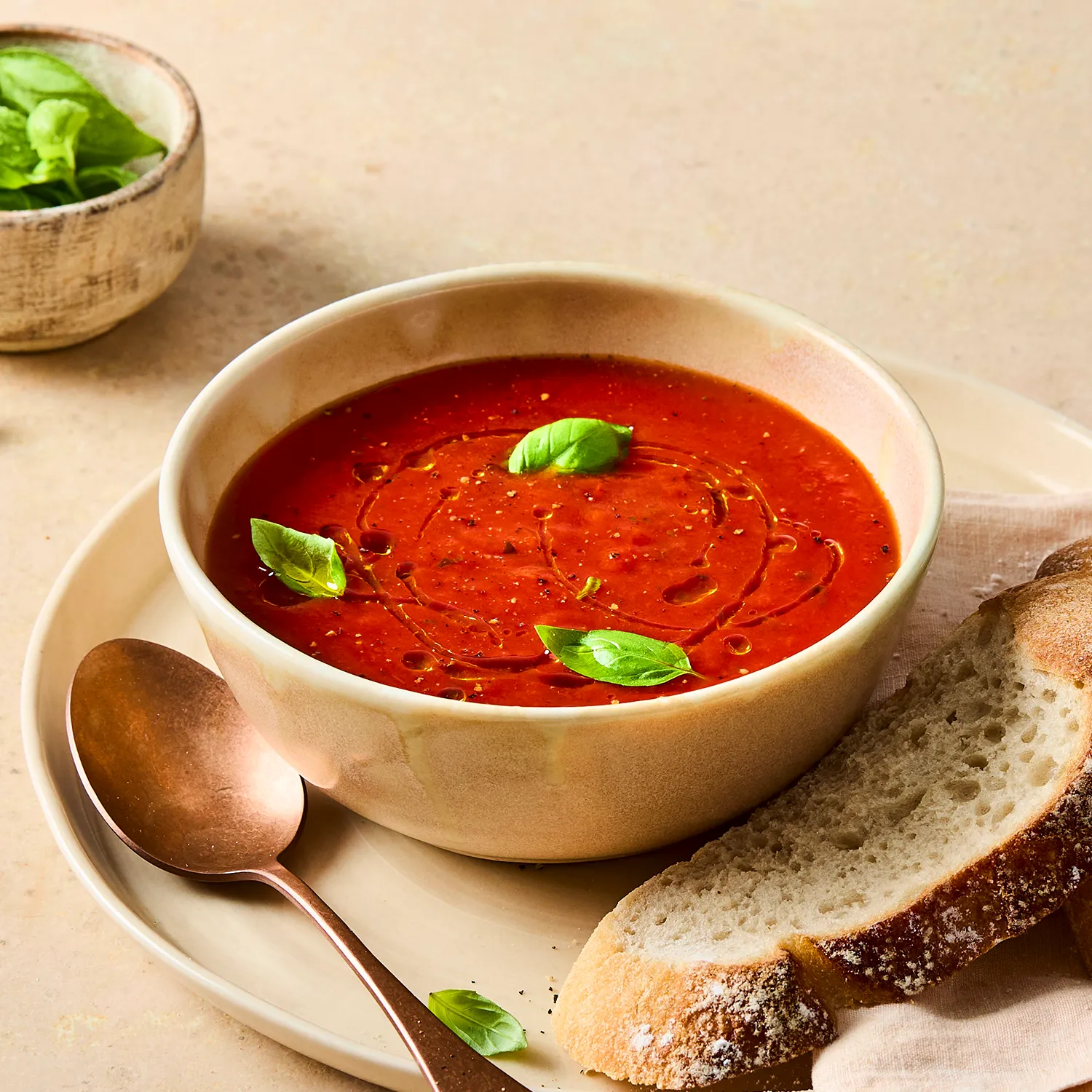A close-up image of a Hovis®  White Sourdough slice on a plate next to a bowl of Tomato and Basil Soup sprinkled with basil leaves.