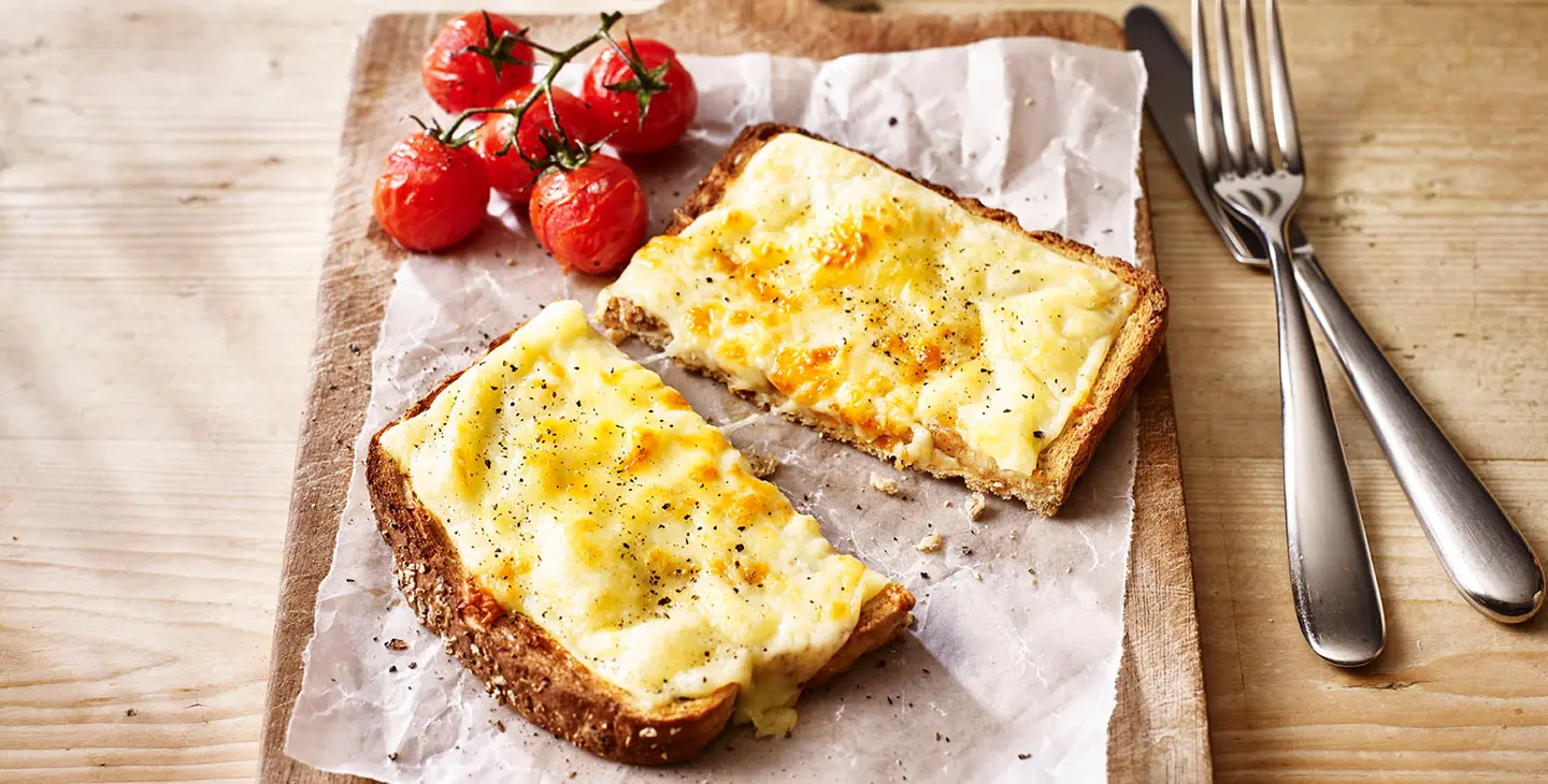 A mouth watering cheese toastie with roasted tomatoes sits on a wooden board in the kitchen.