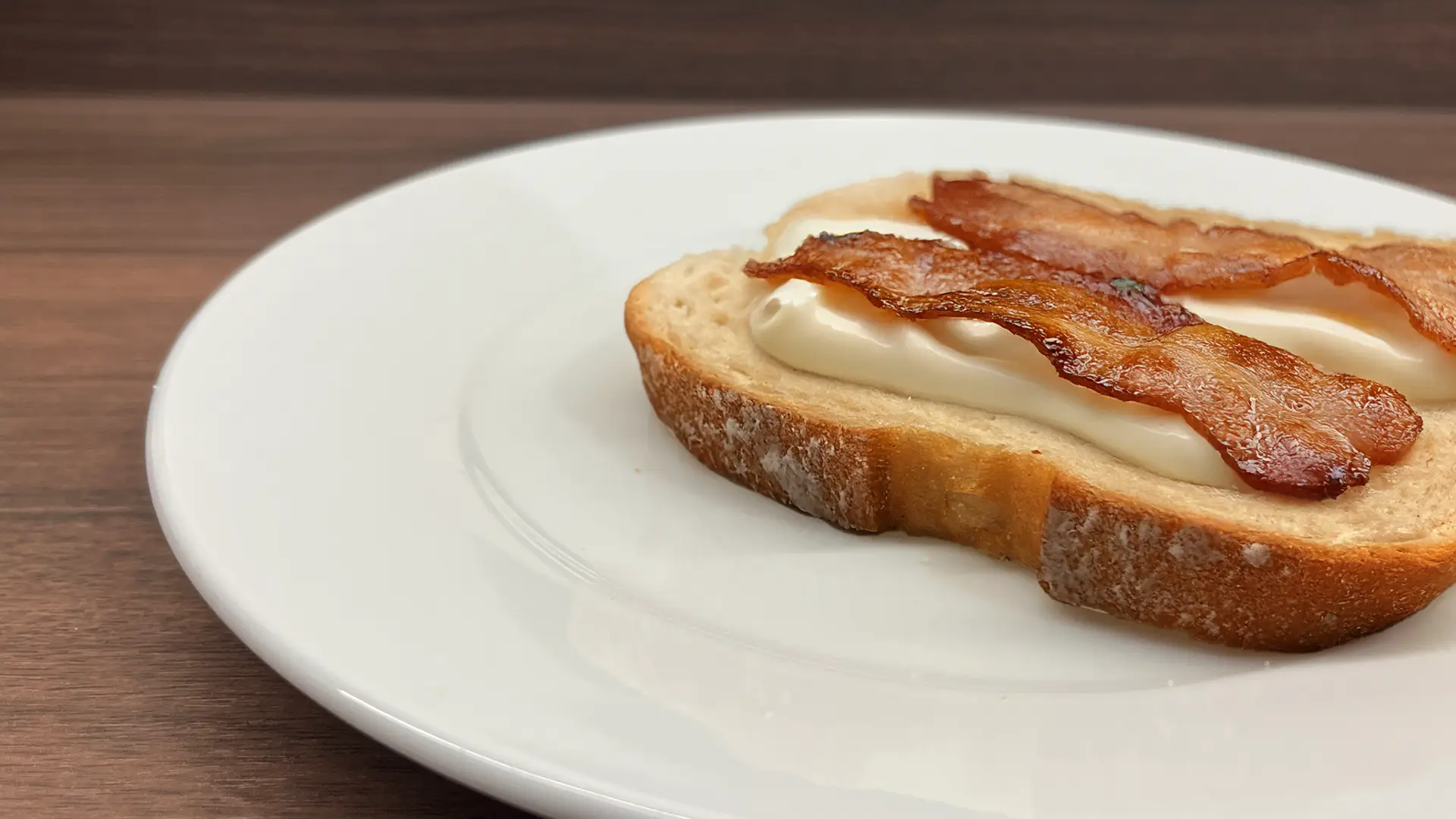 A close up of an open sandwich on a plate topped with mayonnaise and bacon