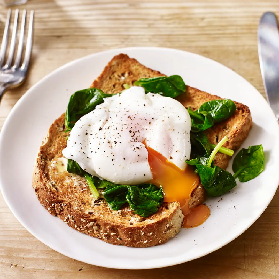 A toasted slice of Hovis Granary Medium Sliced on a plate, topped with wilted spinach and a perfectly poached egg, with the runny yolk spilling over the toast.