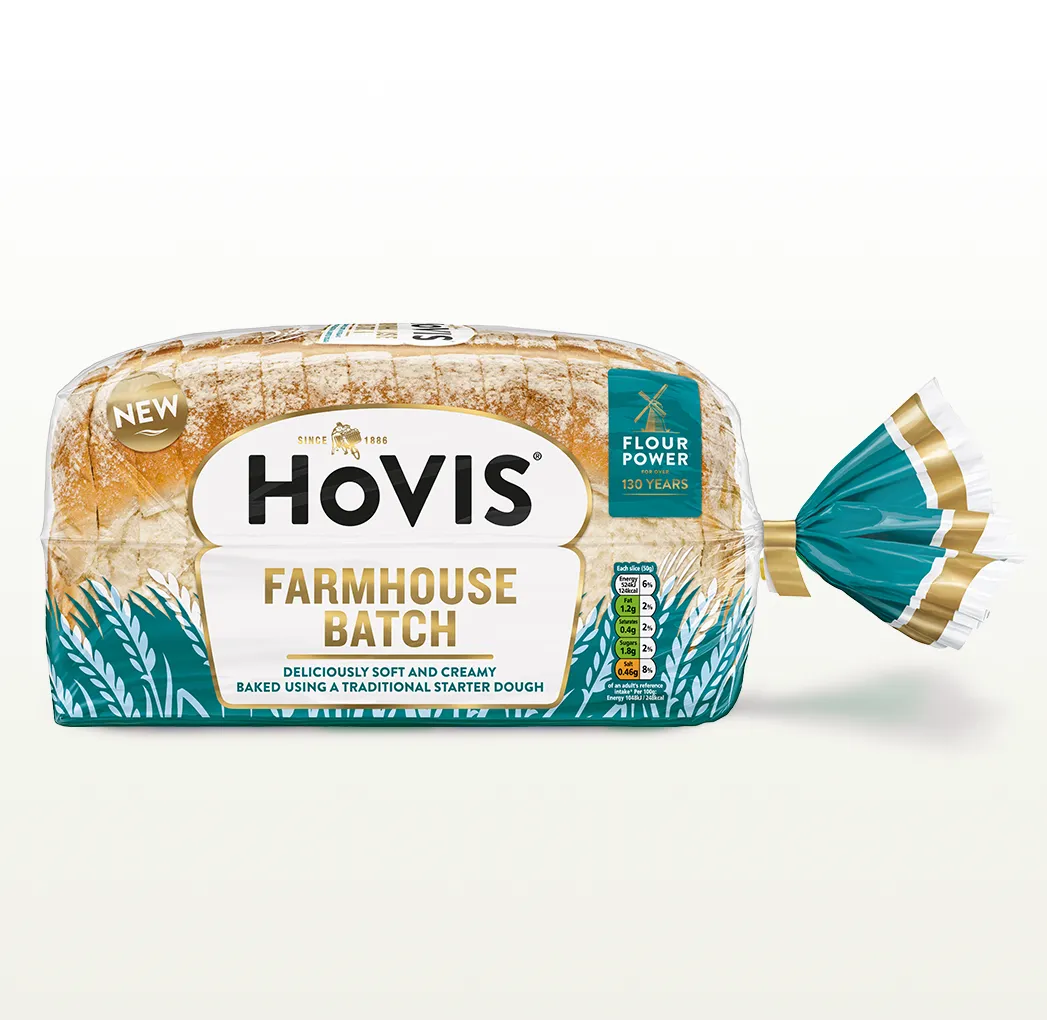 Hovis Farmhouse Batch bread on a white backdrop with a subtle shadow. The packaging is half transparent and half dark teal, decorated with wheats.