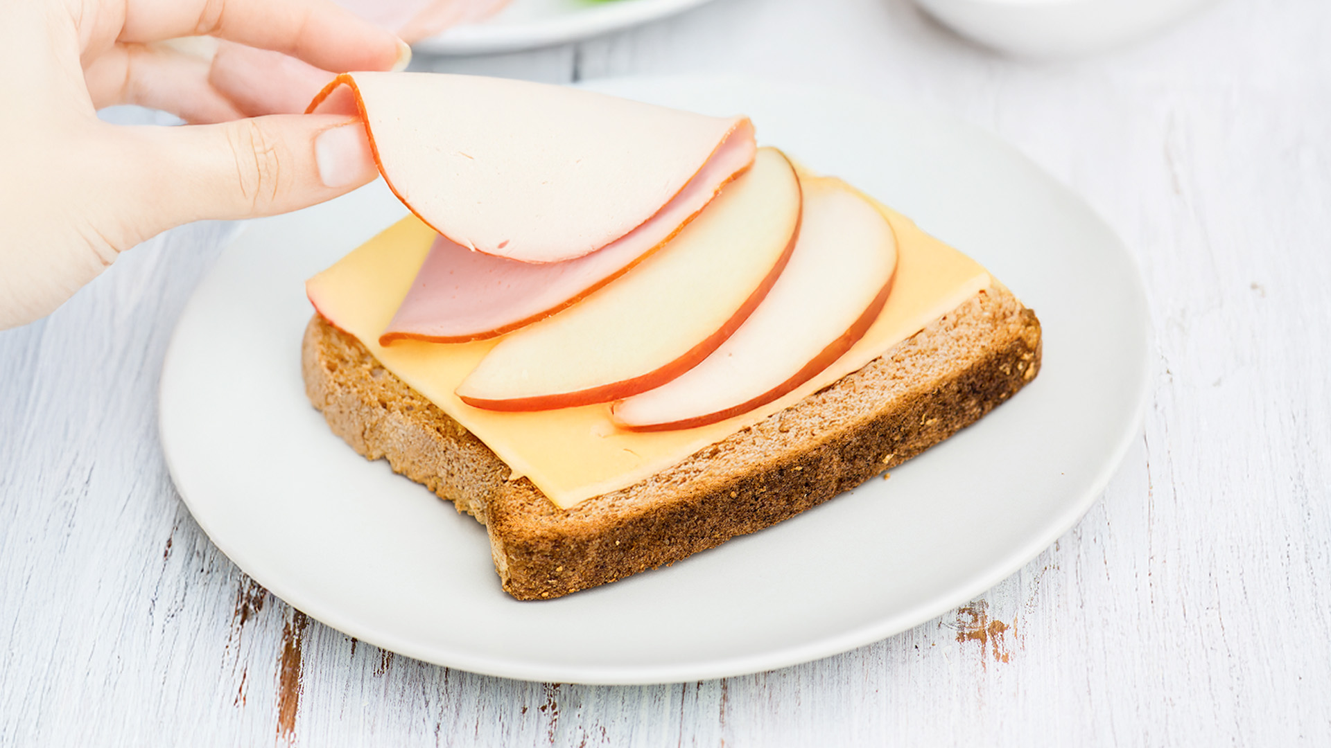 An image of a hand placing turkey slices  on top of a Hovis® Farmhouse Wholemeal with Oats slice that already has cheddar and apple slices on top 