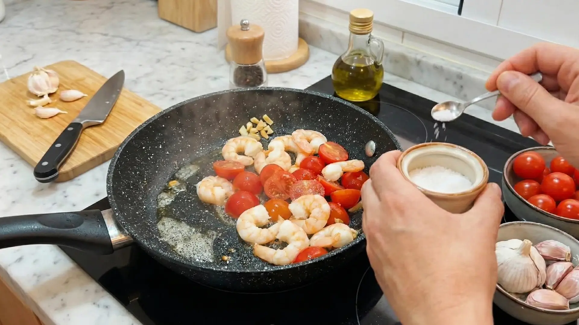 Seasoning prawns, tomatoes, and garlic in a sizzling pan with a spoonful of salt during stovetop cooking.