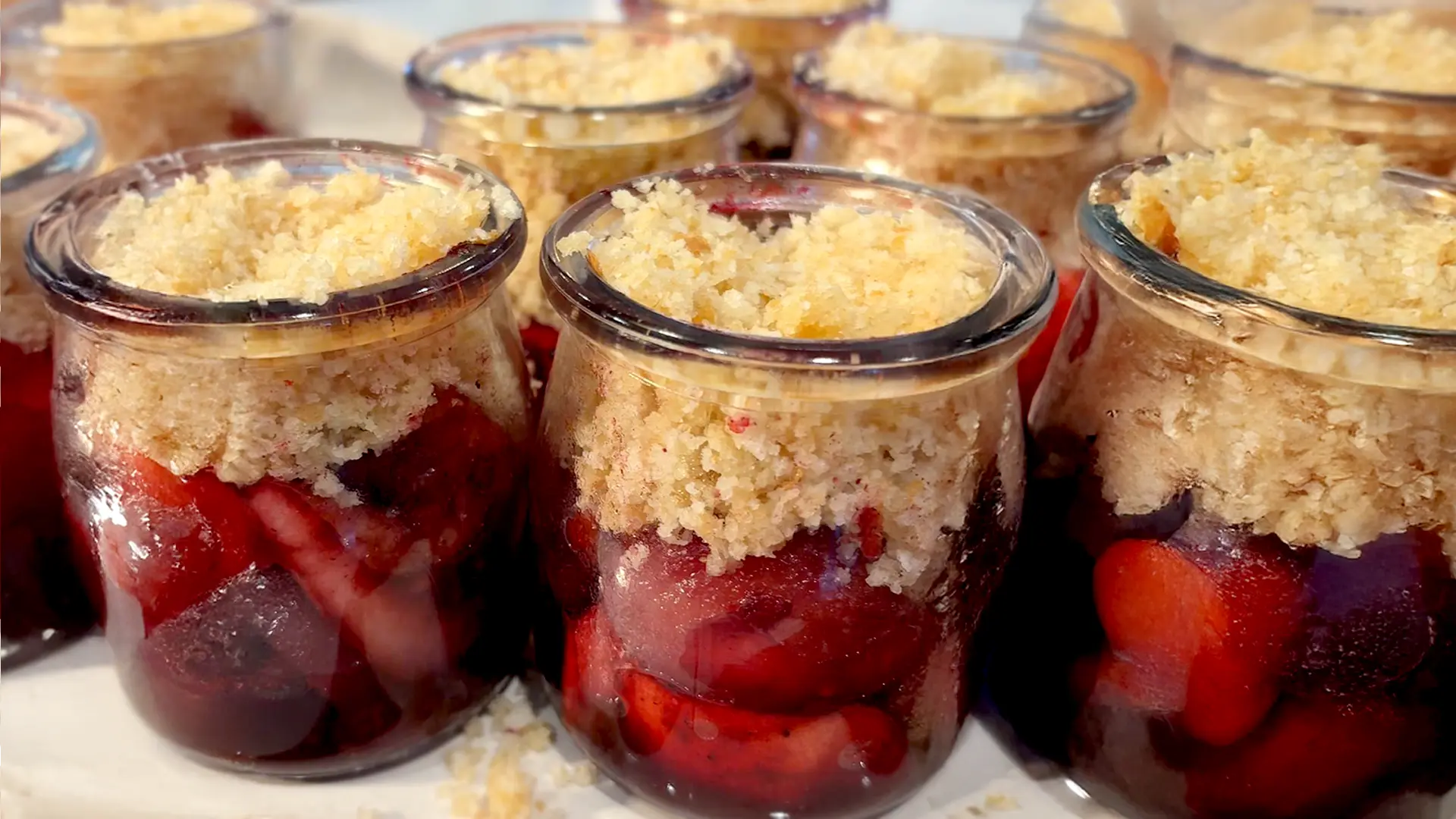 A close-up of small pots filled with uncooked fruit crumble, showing the layers of spiced fruit topped with a buttery Hovis® breadcrumb mixture.