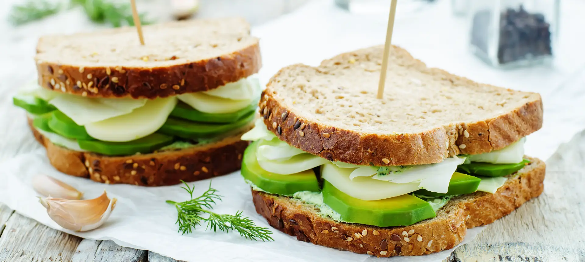 Two sandwiches made with Hovis Seed Sensations Malted Wholegrain bread, filled with sliced cucumber, avocado, cheese, and cream cheese.