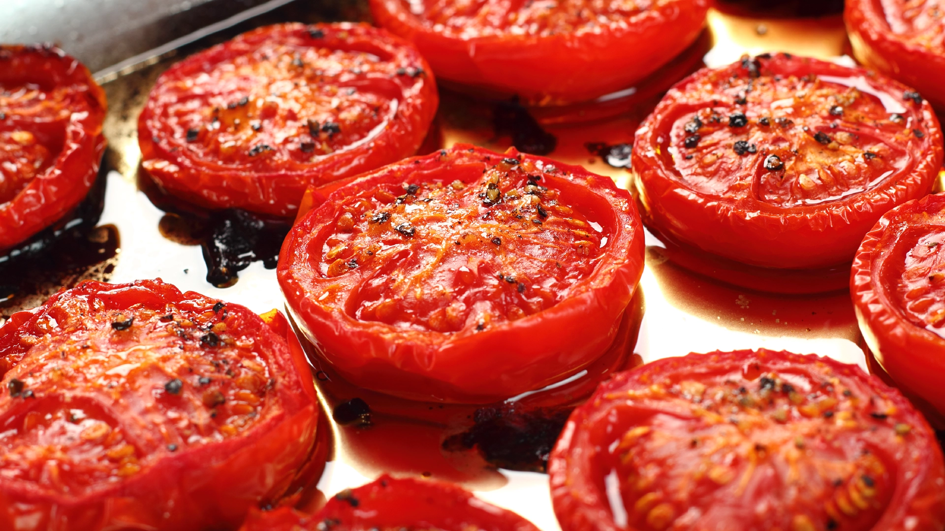 Medium-sized tomatoes, halved and lightly roasted with a drizzle of oil, arranged in a metal tray for baking.