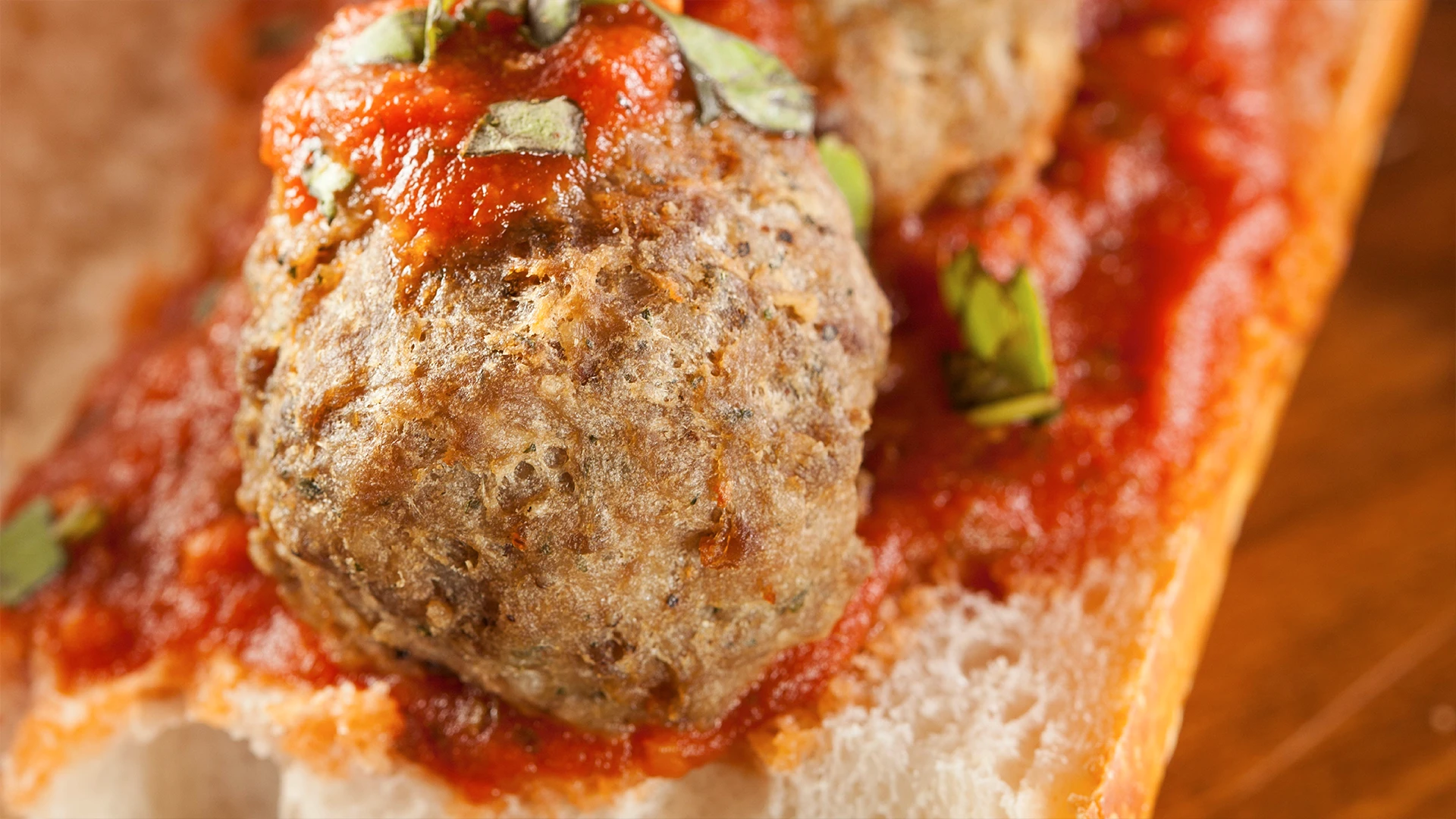 A zoomed in shot of the tomato sauce and beef meatballs sitting on an open sub roll