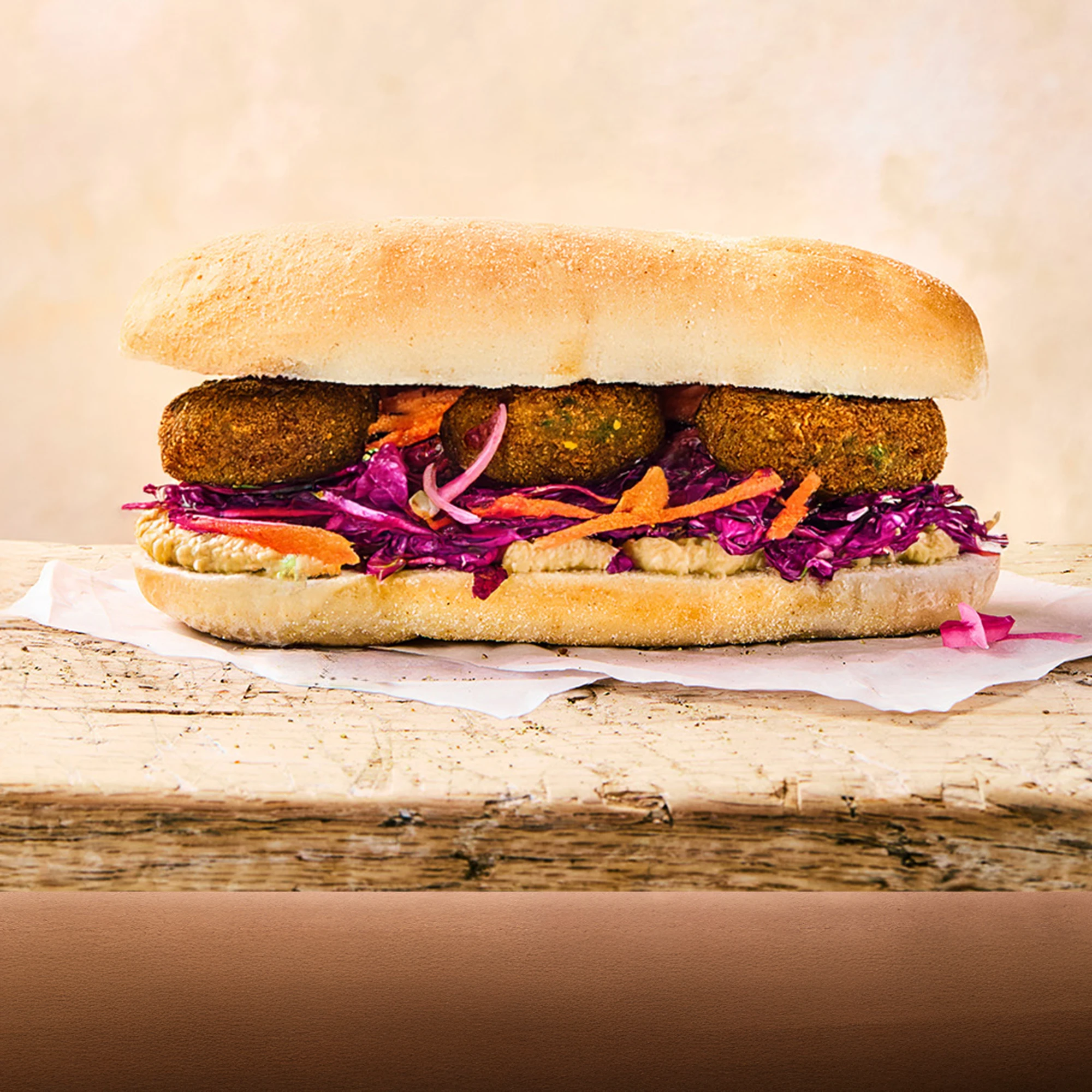 A full falafel, hummus and slaw sub sitting on parchment paper on a wooden surface