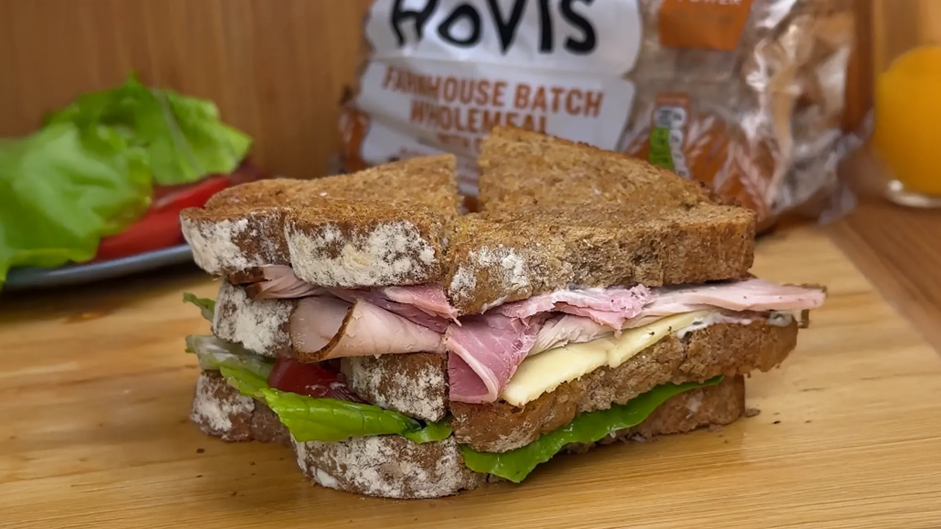 An image of the final Club sandwich with its ingredients spilling out, cut into half triangles on a cutting board. We see the Hovis® Farmhouse Batch Wholemeal loaf in the background.