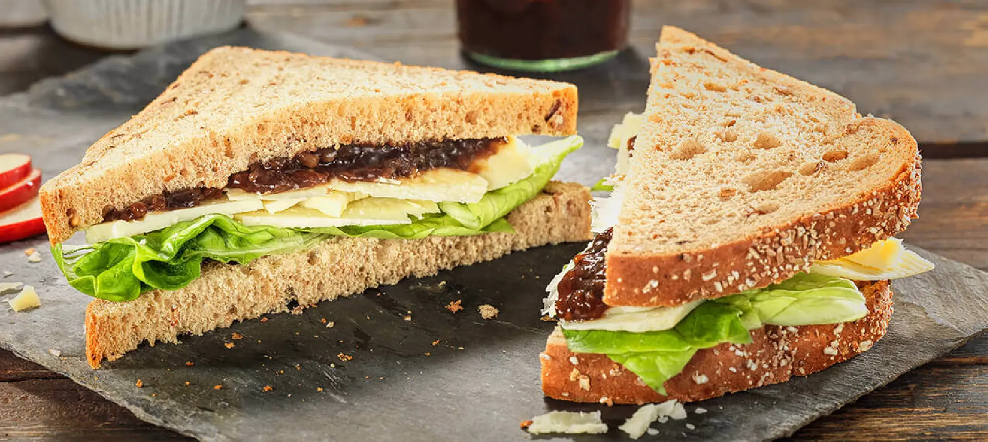 A sandwich made with Hovis Granary Thick Sliced bread, sliced in half and filled with onion chutney, thin slices of cheese, and lettuce leaves.