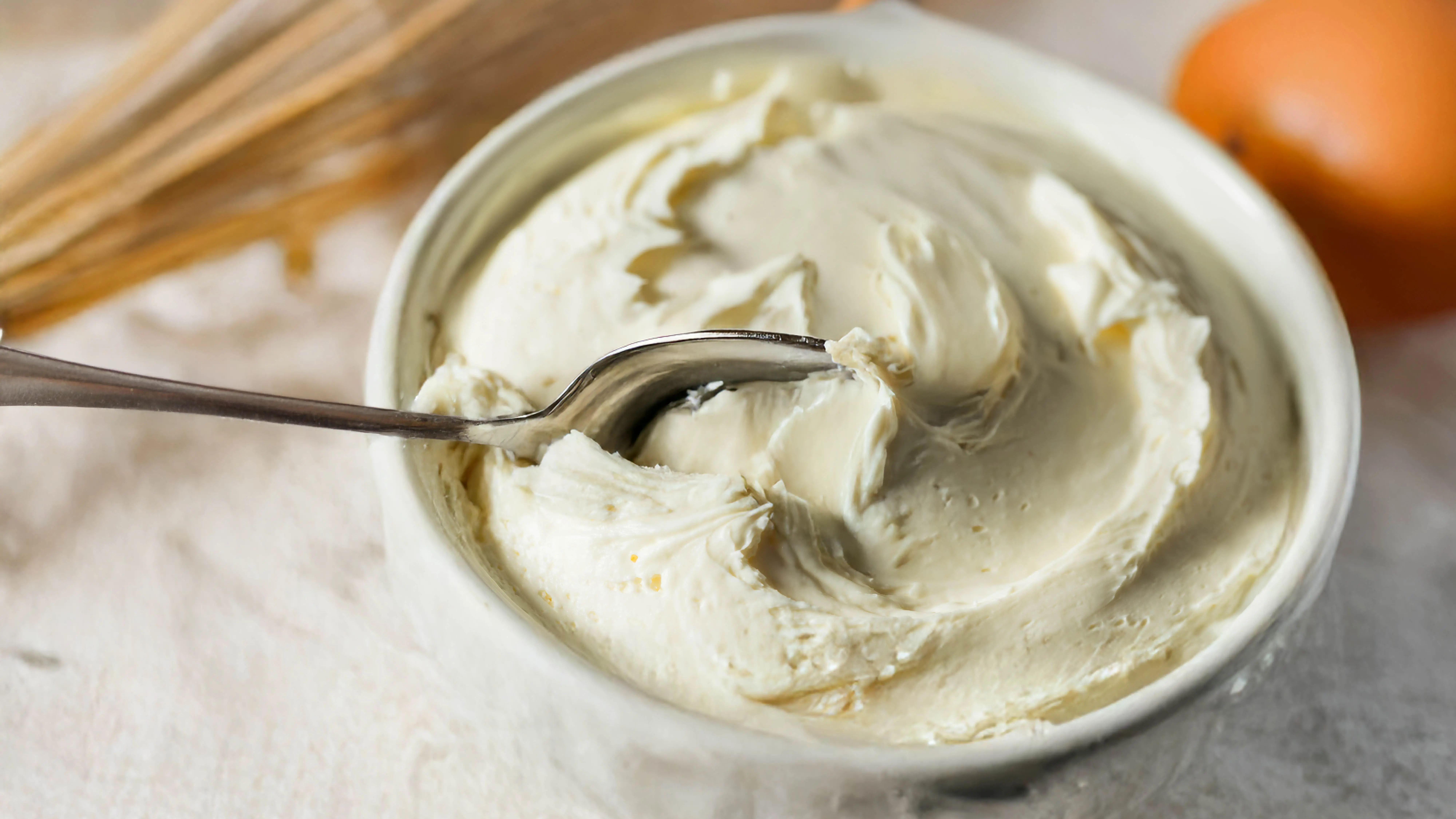 Whipped clotted cream in a small white bowl, with a spoon resting on the side, ready to scoop 