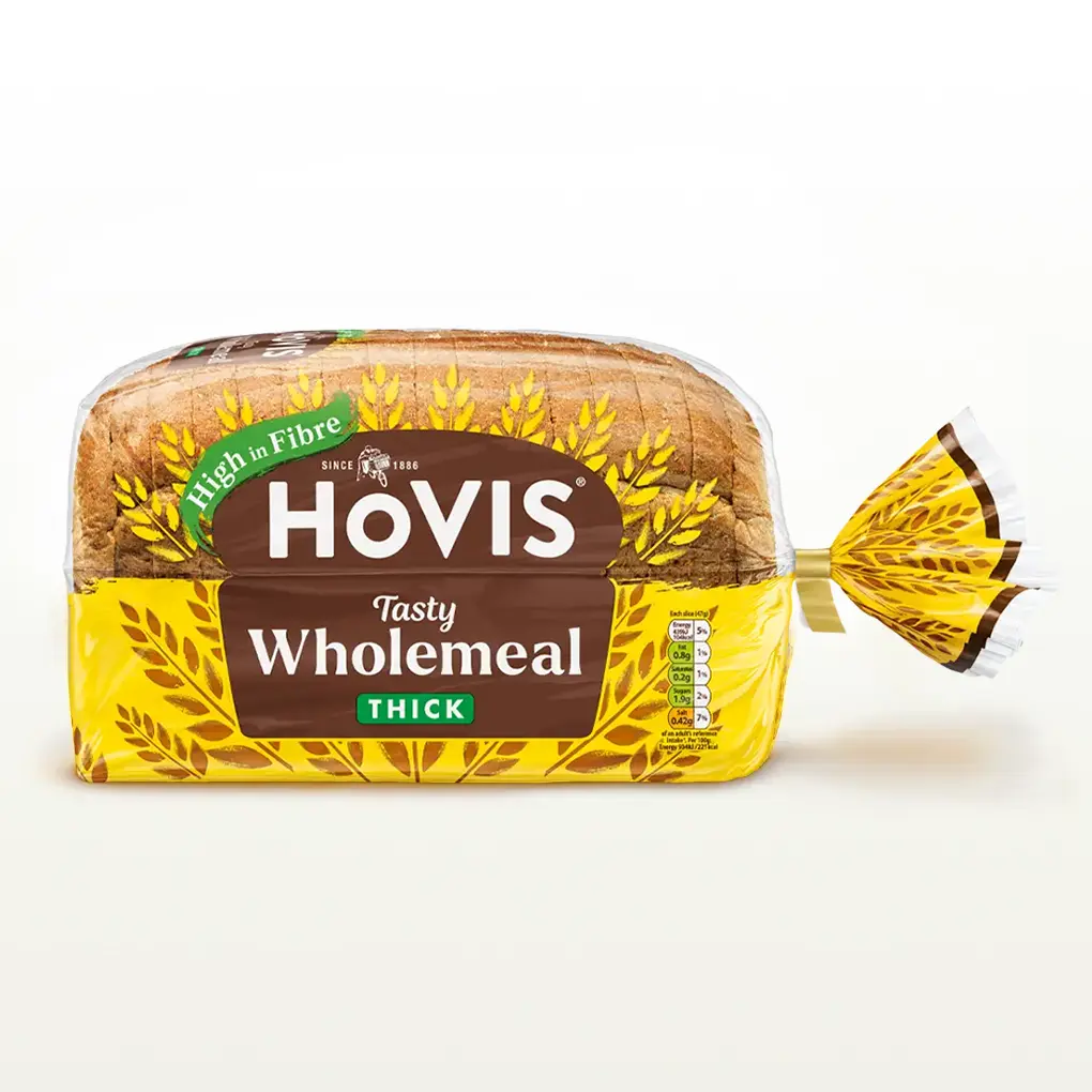 Hovis Tasty Wholemeal Thick Sliced bread on a white backdrop with a subtle shadow. The packaging is half transparent and half yellow, decorated with golden wheats.