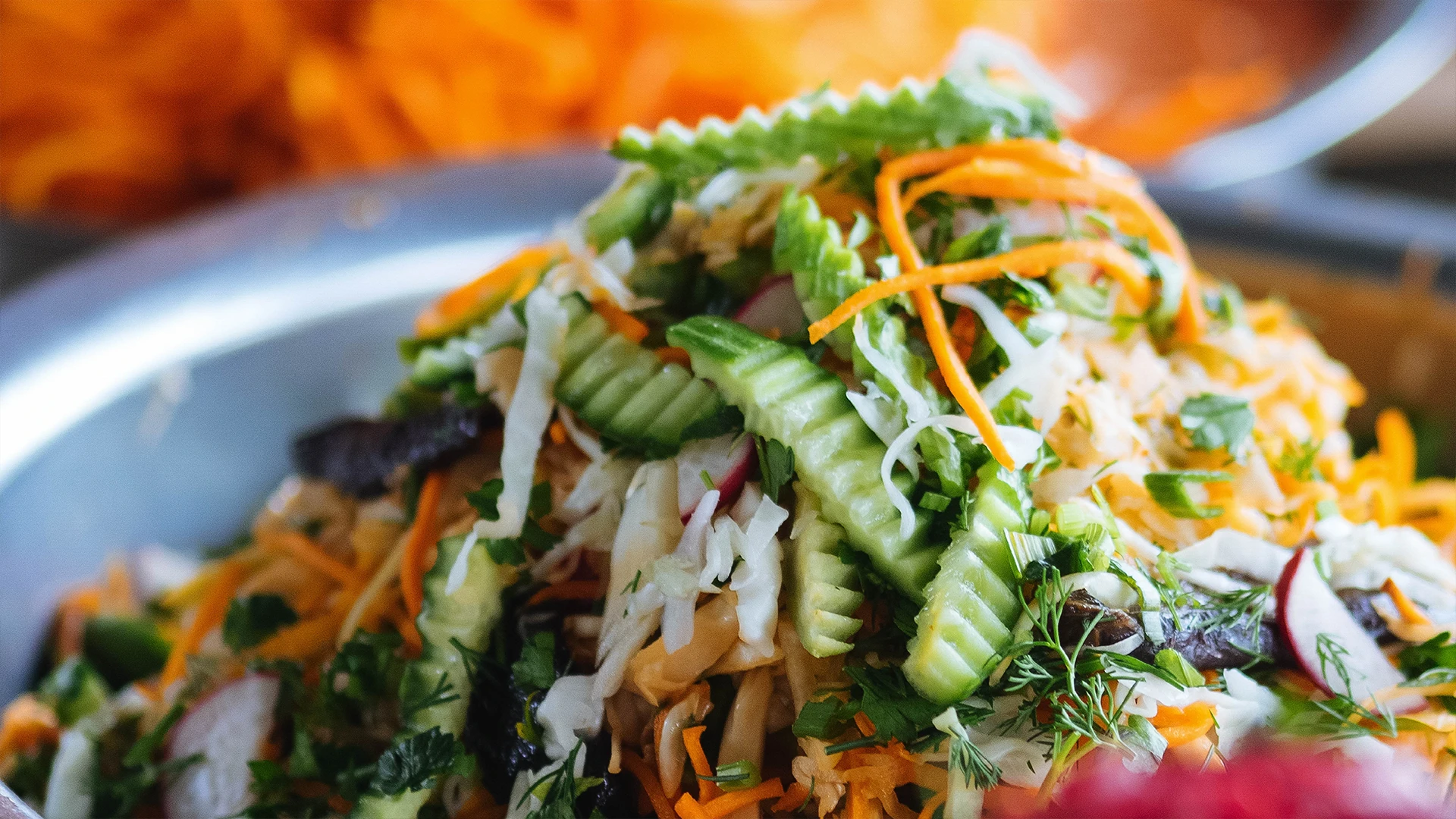 A zoomed in shot of Asian Slaw being prepared containing cucumber, carrot, coriander, mint, and lime juice.
