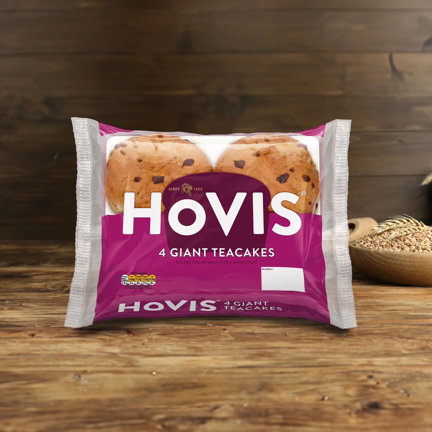 Hovis 4 Teacakes on a wooden table, with a bowl of wheat grains, a wooden scoop, and dried wheat in the background.