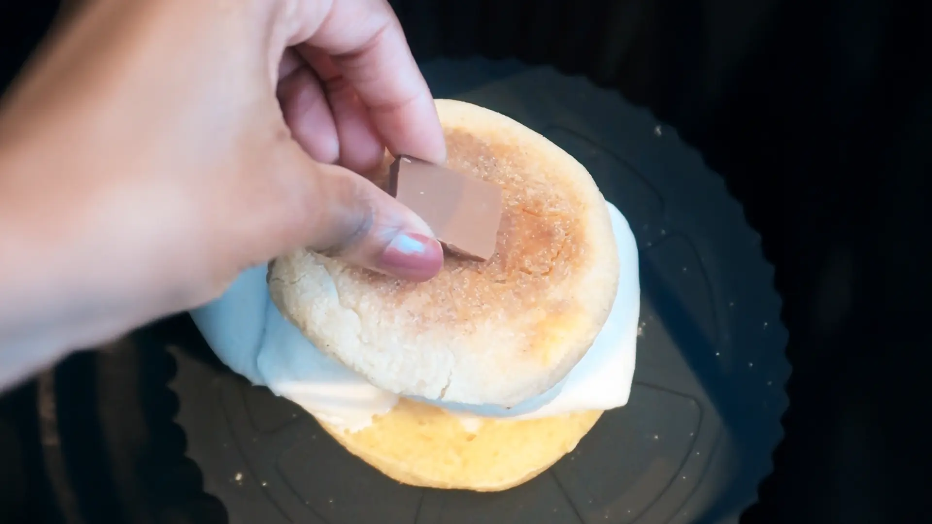 A close-up image of someone adding a small piece of chocolate on top of an English muffin Smores inside an AirFryer. 
