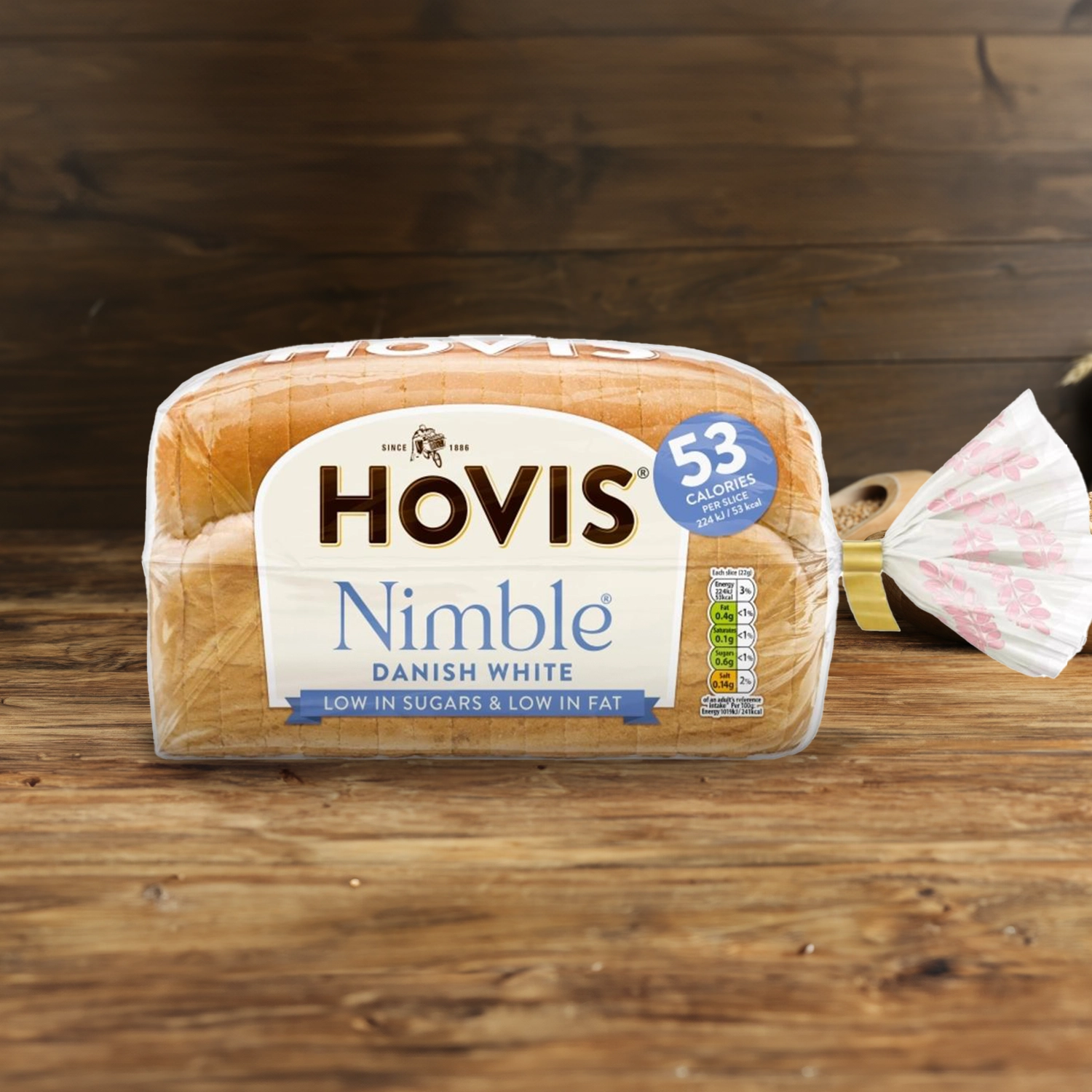Hovis Nimble Danish White on a wooden table, with a bowl of wheat grains, a wooden scoop, and dried wheat in the background.