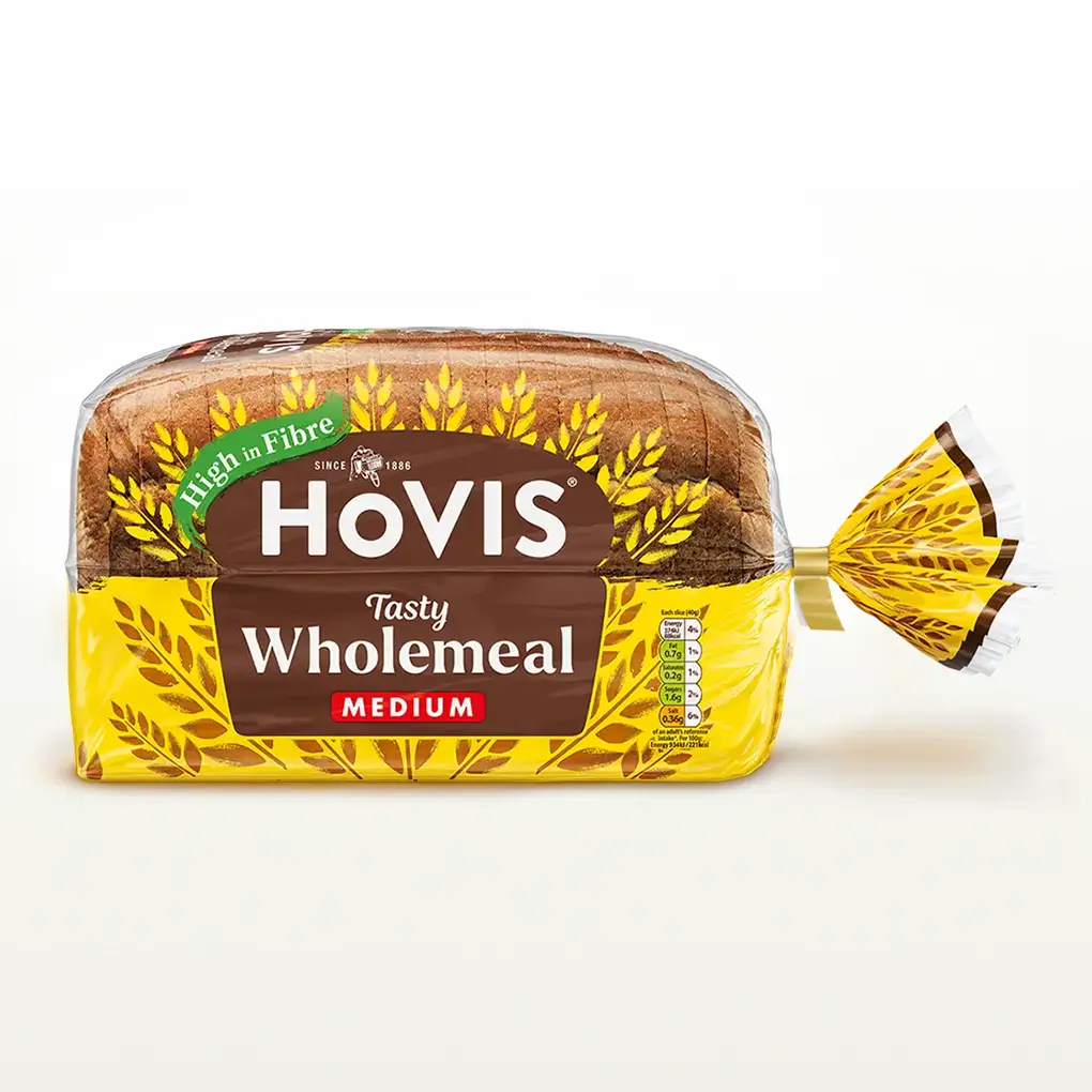 Hovis Tasty Wholemeal Medium Sliced bread on a white backdrop with a subtle shadow. The packaging is half transparent and half yellow, decorated with golden wheats.